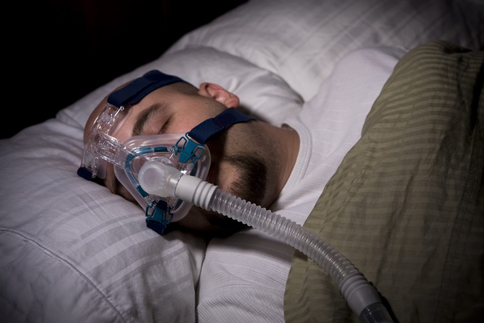 Man sleeping while wearing a CPAP mask for sleep apnea.
